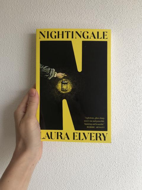 The Nightingale book cover; it has a large black N on a bright yellow background. Inside the N is an illustration of an arm holding a lamp.
